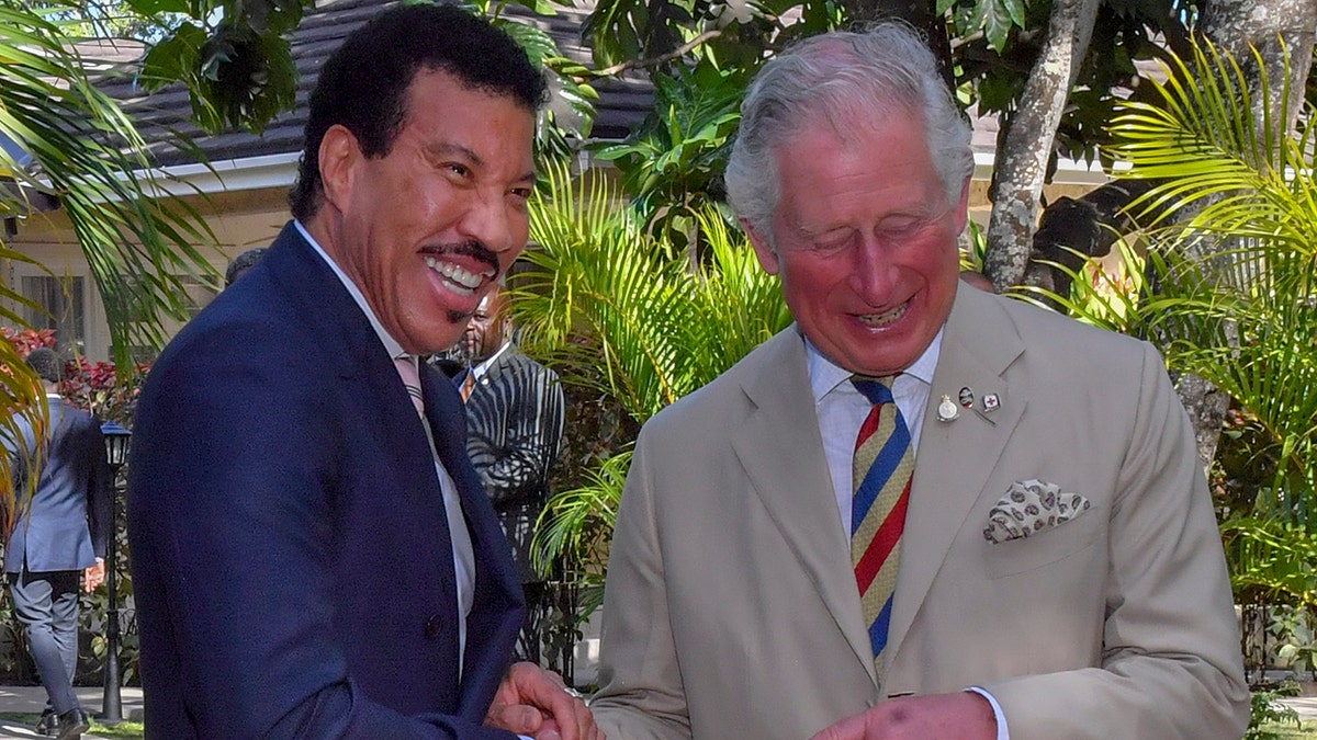 Lionel Richie in a blue jacket laughs with the then Prince Charles in a light tan suit and striped tie while together in Barbados