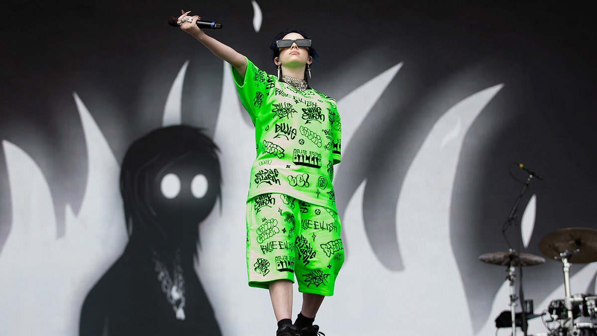 Billie Eilish holds her microphone out to the audience in a green matching shorts and t-shirt set in Middlesbrough, England