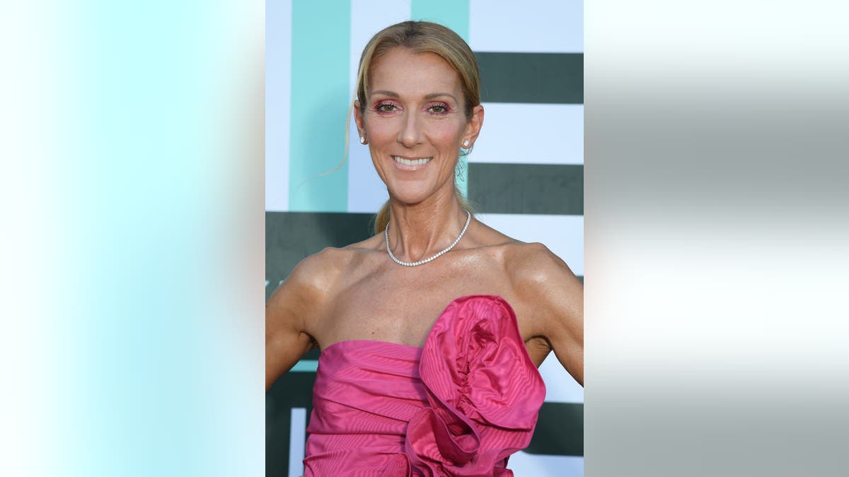 Celine Dion smiles on the red carpet in a hot pink strapless gown with a flower on one side in Paris