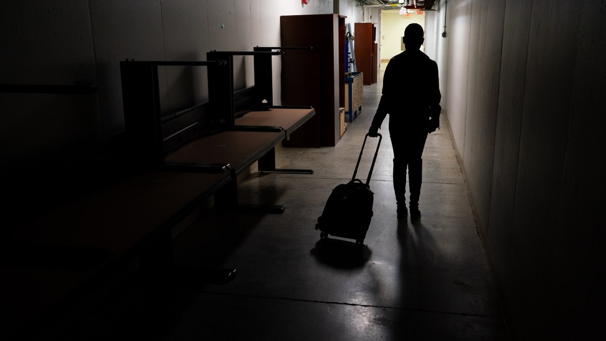 An NC State students walks through a hallway with a suitcase