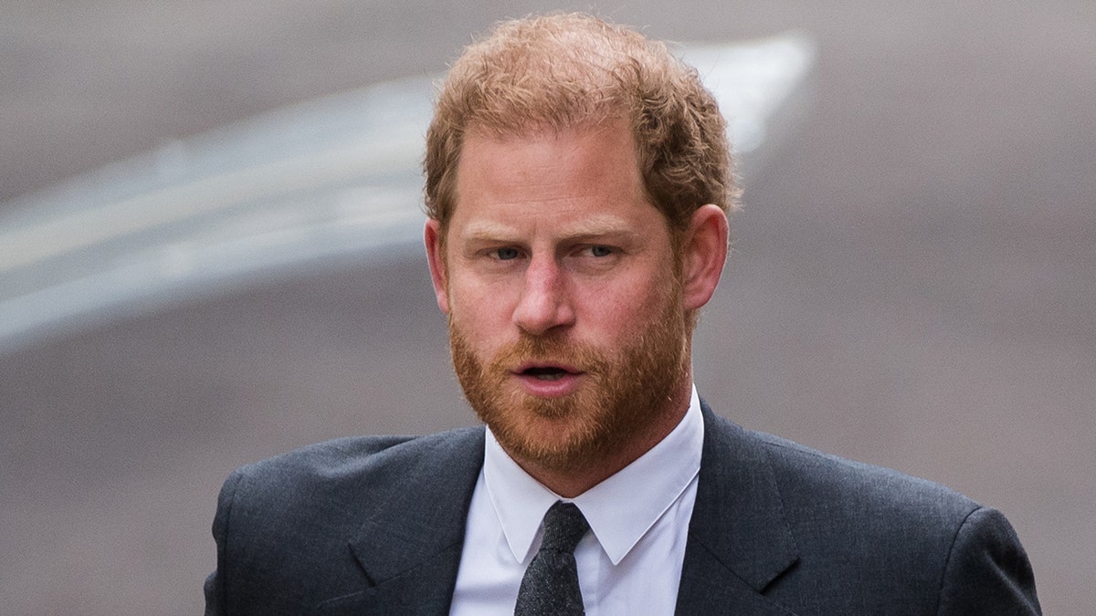Prince Harry in a dark grey suit and tie looks off to his left while walking into High Court