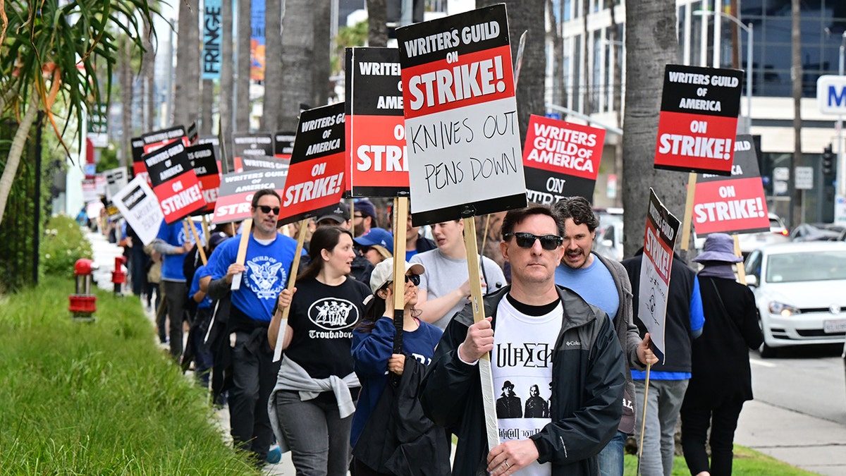 Writer Eric Heisserer holds his writers strike sign on the fourth day of the writers strike in front of Netflix in Hollywood, followed by many other individuals