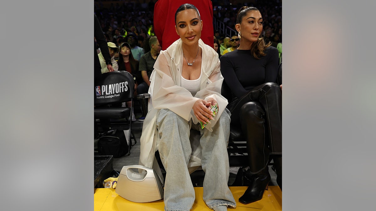 Kim Kardashian wears a tank top, transparent poncho, flare jeans and denim shoes courtside at the Lakers