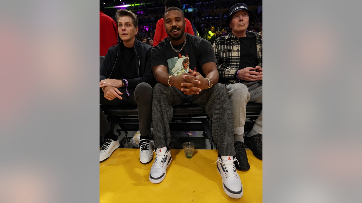 Michael B. Jordan smiles for a photo courtside, wearing a black Princess Mononoke shirt at the Laker's game