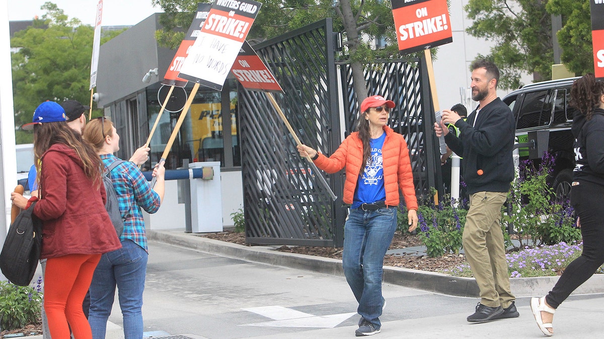 Justine Bateman in a red hat, blue shirt, and red jacket protests in Hollywood during the Writer's Strike