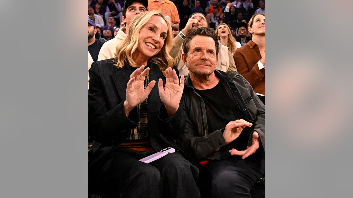 Michael J. Fox looks up courtside at the Knick game in New York, sitting next to his wife Tracy who has her hands upwards