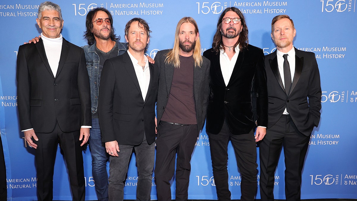 The Foo Fighters stand next to each other in front of a blue backdrop at the American Museum of Natural History Gala