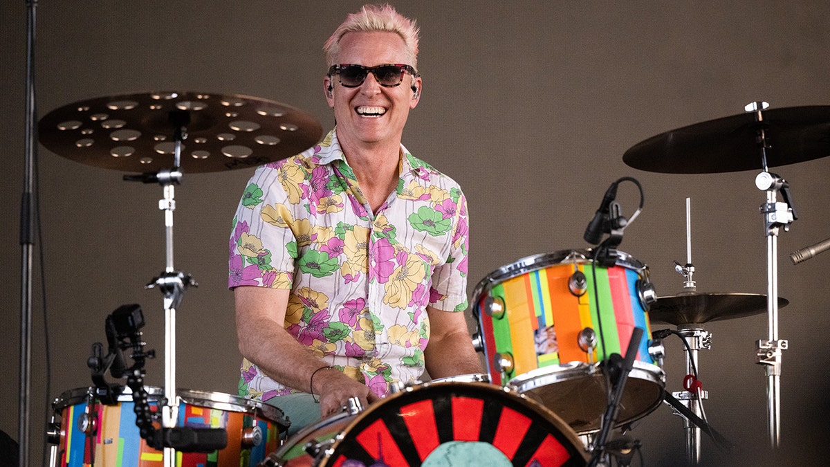 Josh Freese in a colored patterned shirt smiles with sunglasses on behind a set of drums playing at Coachella