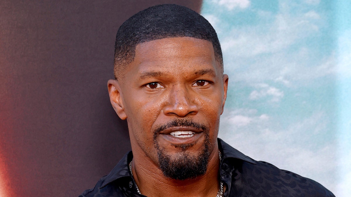 Jamie Foxx smiles on the carpet in a black shirt in Los Angeles