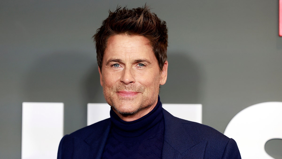 Rob Lowe soft smiles in a black turtleneck and blue suit at the premiere of his Netflix show "Unstable"