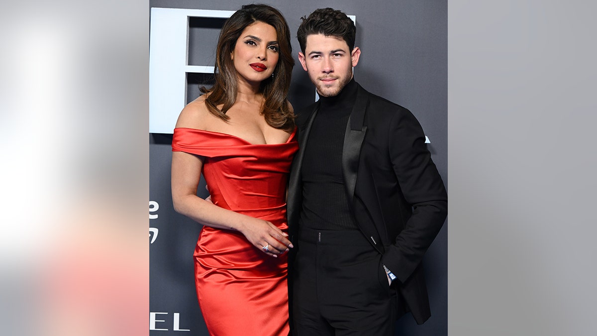 Priyanka Chopra in a red form-fitting off-the-shoulder gown poses on the red carpet with husband Nick Jonas in all black at the premiere of the "Citadel" in England