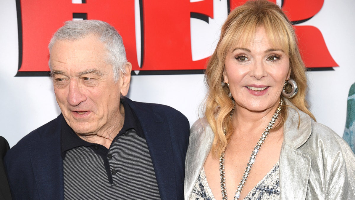 Robert De Niro looks to his right on the red carpet of his new film "About My Father" with co-star Kim Cattrall in a sparkly outfit with a deep V cut