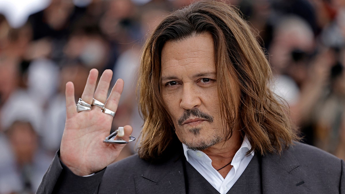 Johnny Depp holds up his right hand with lots of silver rings and waves to the crowd in Cannes with a slight smirk/smile on his face