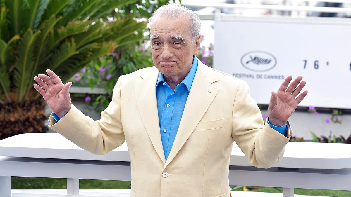 Martin Scorsese with his arms outstretched in a tan suit and bright blue button down at Cannes Film festival