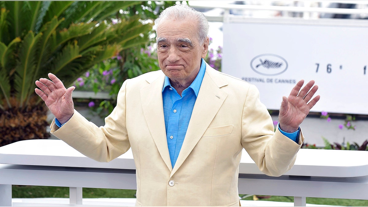 Martin Scorsese with his arms outstretched in a tan suit and bright blue button down at Cannes Film festival