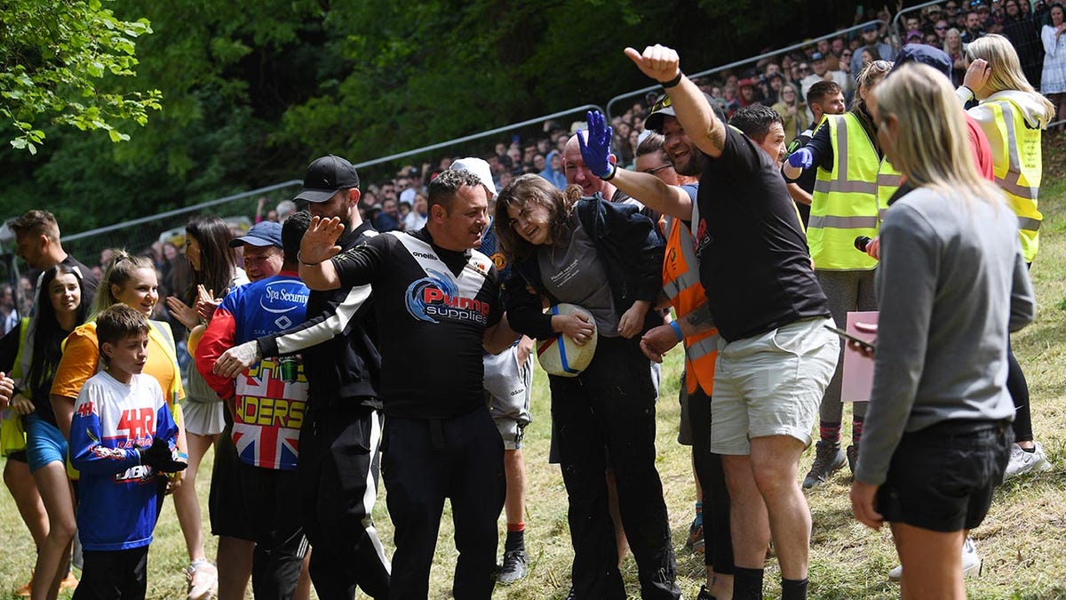 A woman is helped up after winning a cheese rolling race