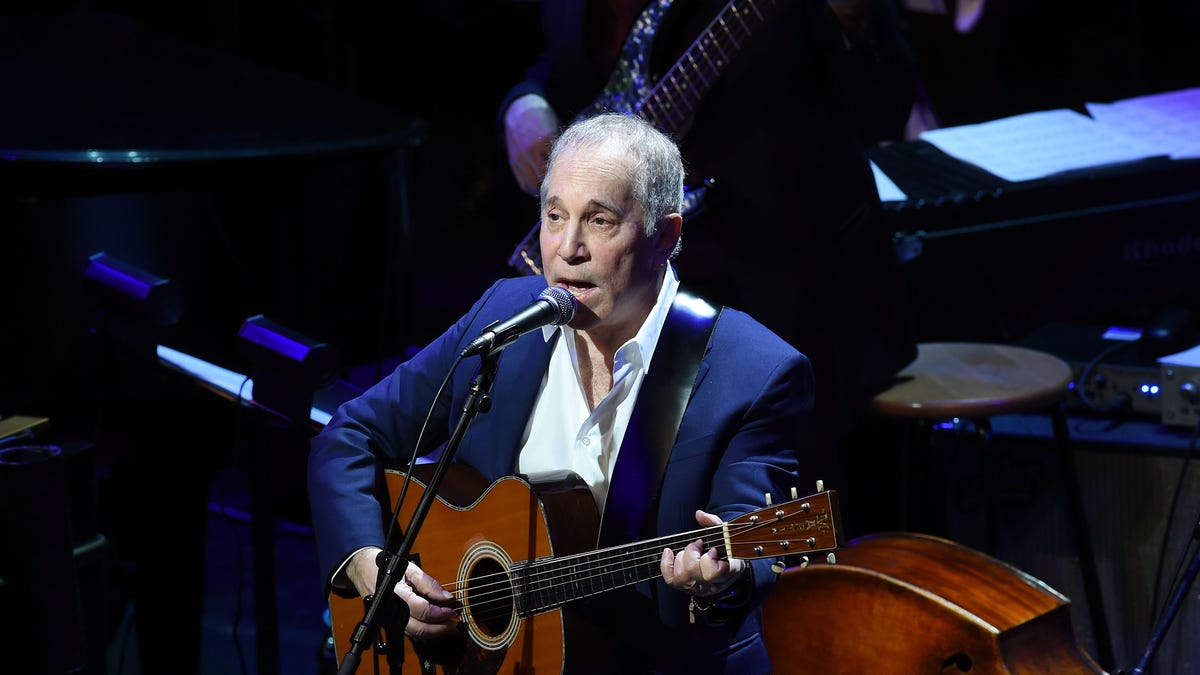 Paul Simon performing with a guitar on stage in 2015.