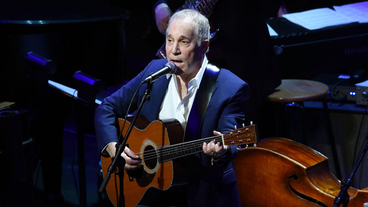 Paul Simon performing with a guitar on stage in 2015.