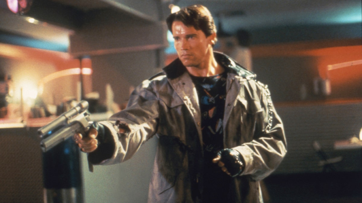 Arnold Schwarzenegger holding a weapon in a scene from "Terminator," where he is wearing a brown leather jacket