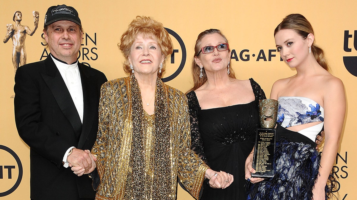 Todd Fisher in a black suit and cap holds mother Debbie Reynold's hand in a gold suit, holding the hand of daughter Carrie Fisher in black, with her daughter Billie Lourd posing in a printed dress with cut-outs holding a SAG Award