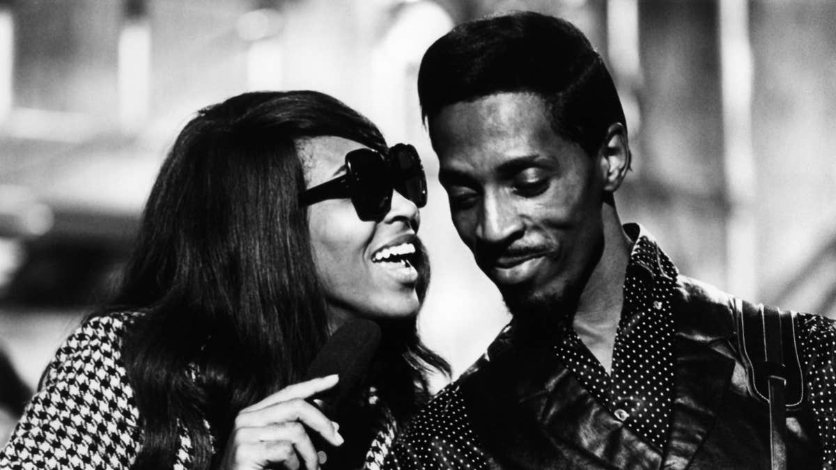 Tina Turner performs wearing sunglasses with Ike Turner in black and white photo.