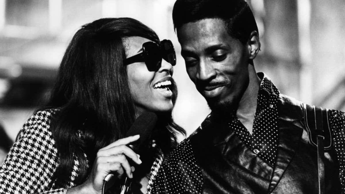 Tina Turner performs wearing sunglasses with Ike Turner in black and white photo.
