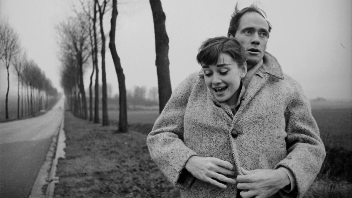 Mel Ferrer envelopes his wife Audrey Hepburn, buttoning her up in his coat, in a picture taken outside Paris in 1956