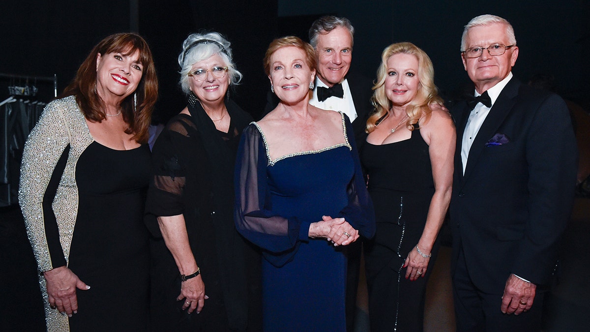 The cast of the sound of music wearing various shades of black and navy posing together for a photo