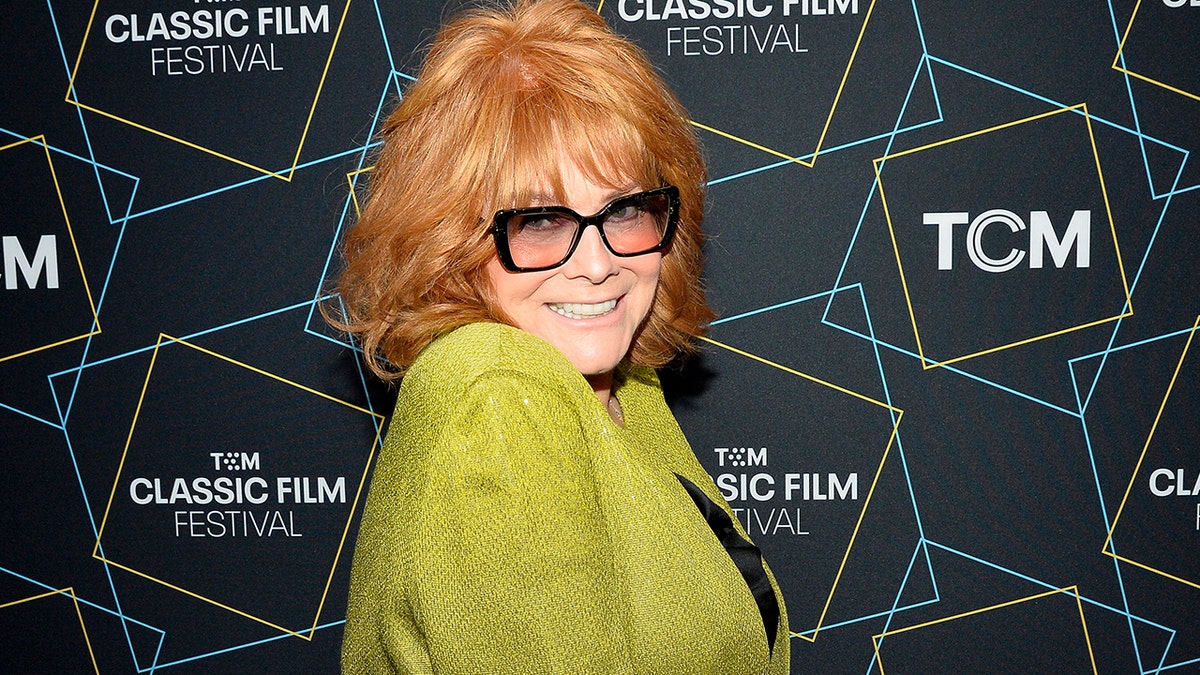A close-up of Ann-Margret smiling wearing a bright green blazer and black shirt