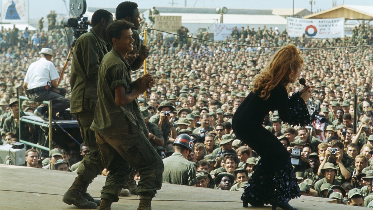 Troops dancing on stage with Ann-Margret who is singing in bell bottoms