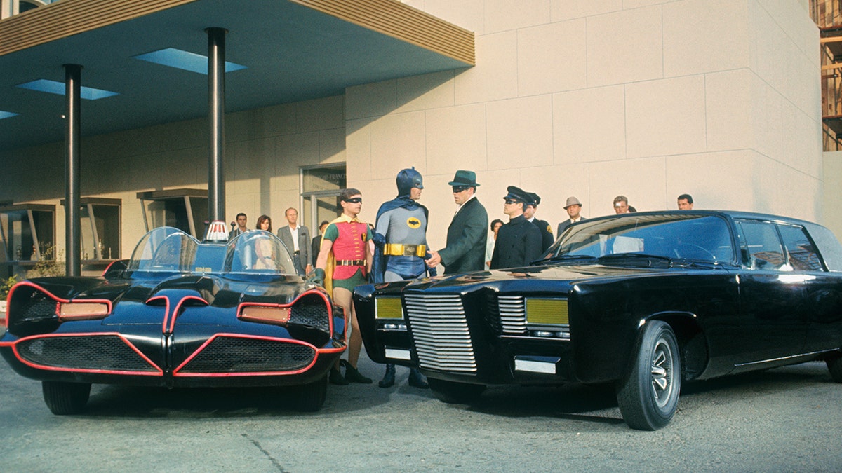 The cast of The Green Hornet and Batman in costume next to cars