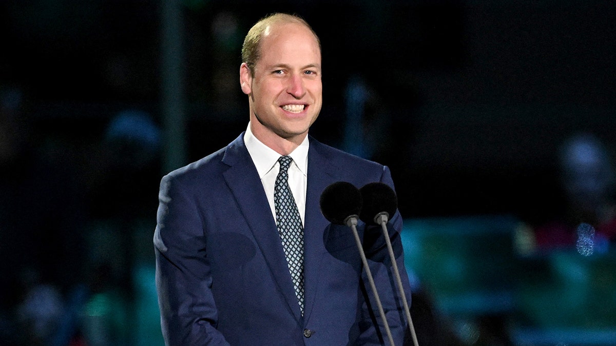 Prince William smiling on stage wearing a blue suit and tie