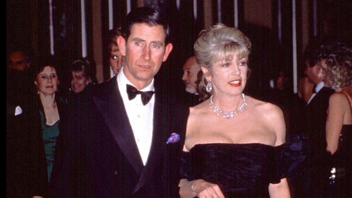 Prince Charles in a suit and bowtie accompanied by Dale Tryon in a low cut black dress with jewels