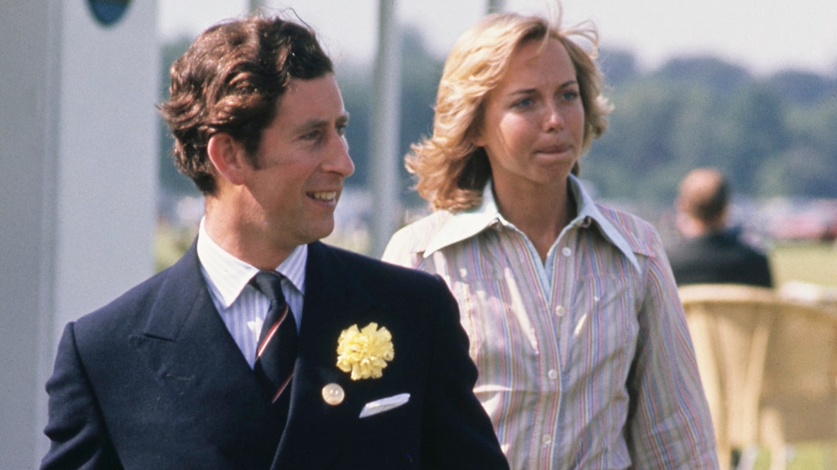 Prince Charles in a dark suit and tie walking in front of Davina Sheffield who is wearing a stripe pastel blouse