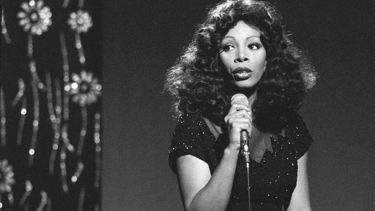 A black and white photo of Donna Summer holding a mic