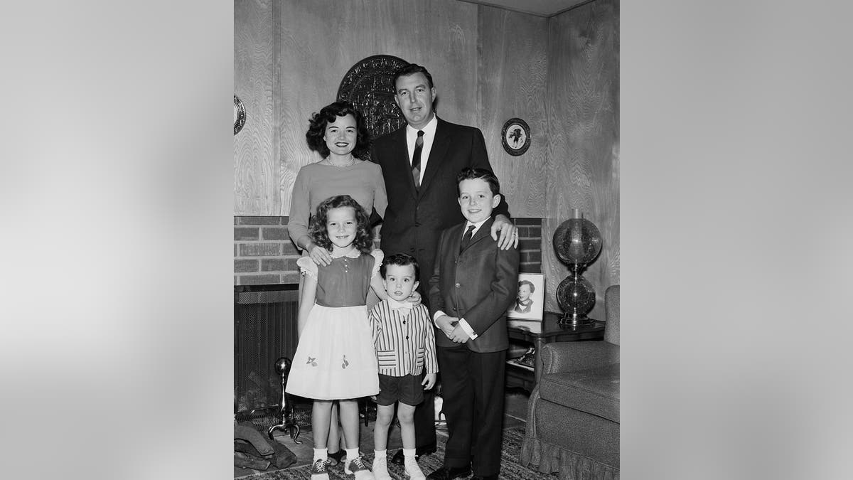 A formal portrait of Jerry Mathers in a suit posing with his family at home during 1960