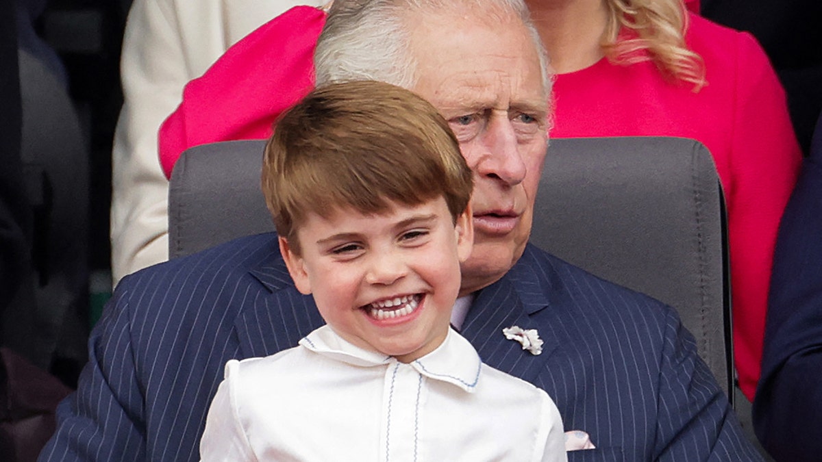 Prince Louis smiling and wearing a white shirt sitting on his grandfather king charles lap