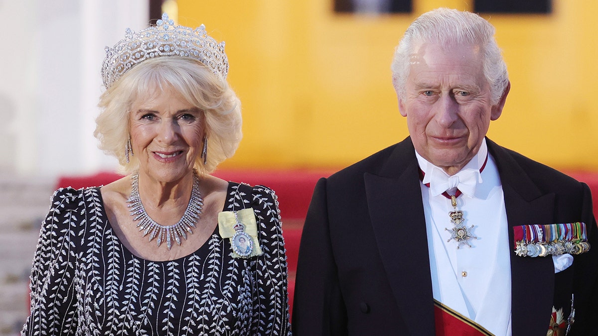 Queen Camilla in a black and white dress with a tiara next to King Charles in a suit