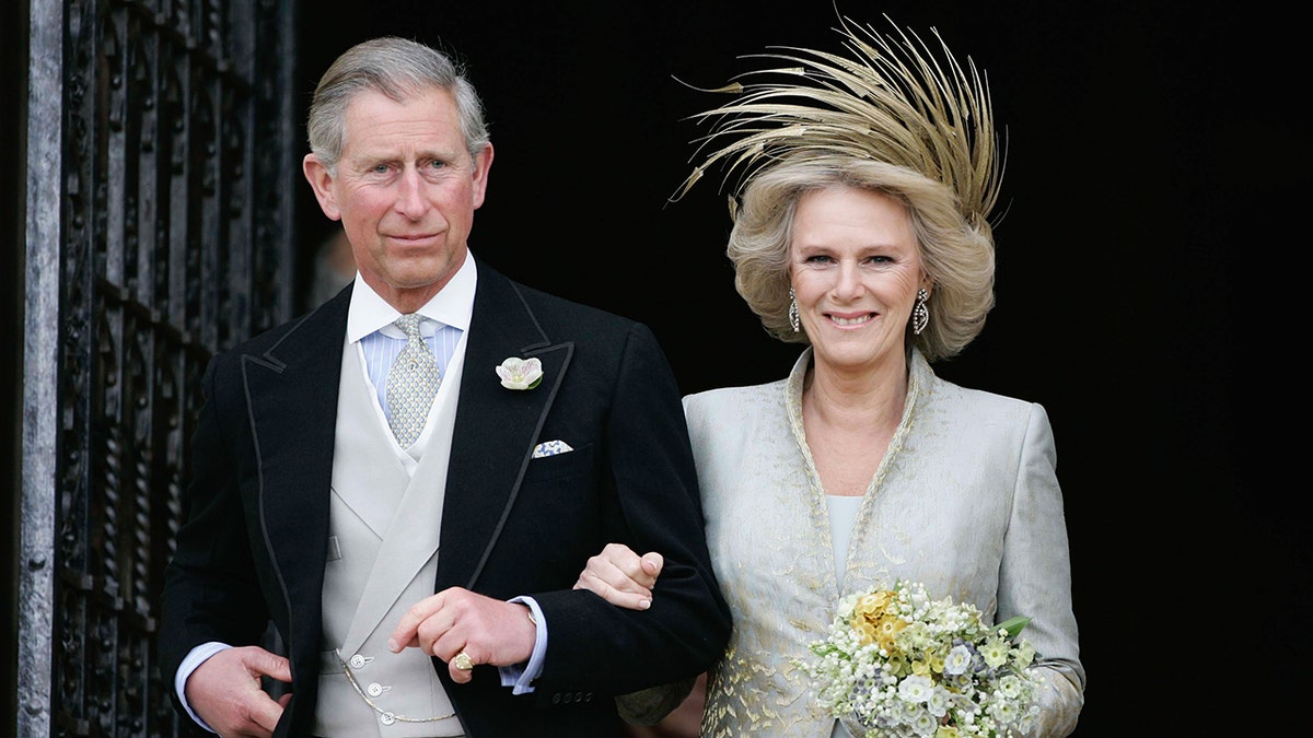 King Charles in a grooms suit and Camilla in a bridal gown with a golden fascinator on their wedding day
