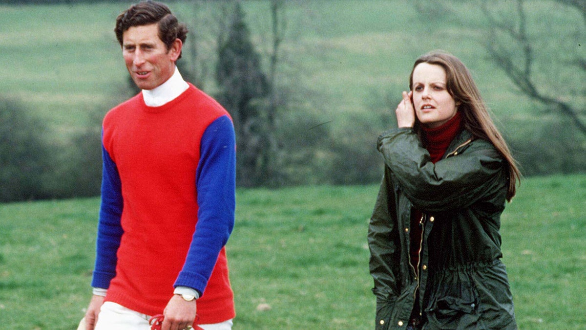 Prince Charles wearing a blue and red sweater walking on a field with Lady Jane in a green coat