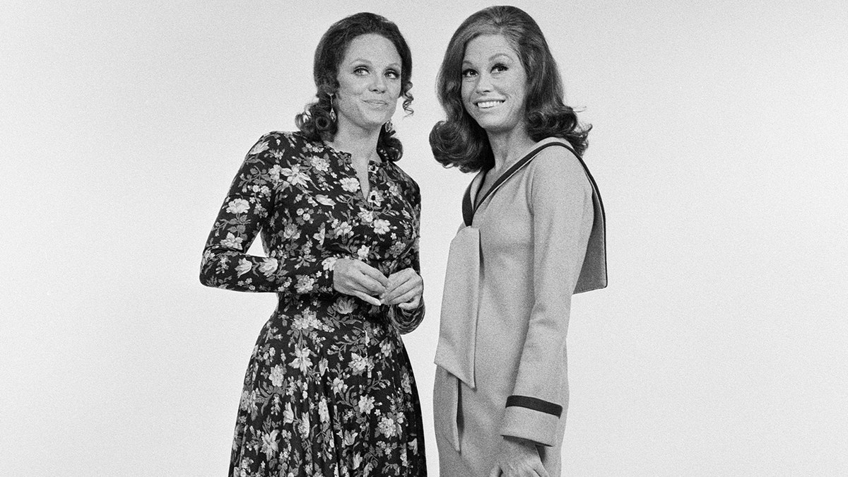 Valerie Harper leaning in to Mary Tyler Moore wearing a floral dress