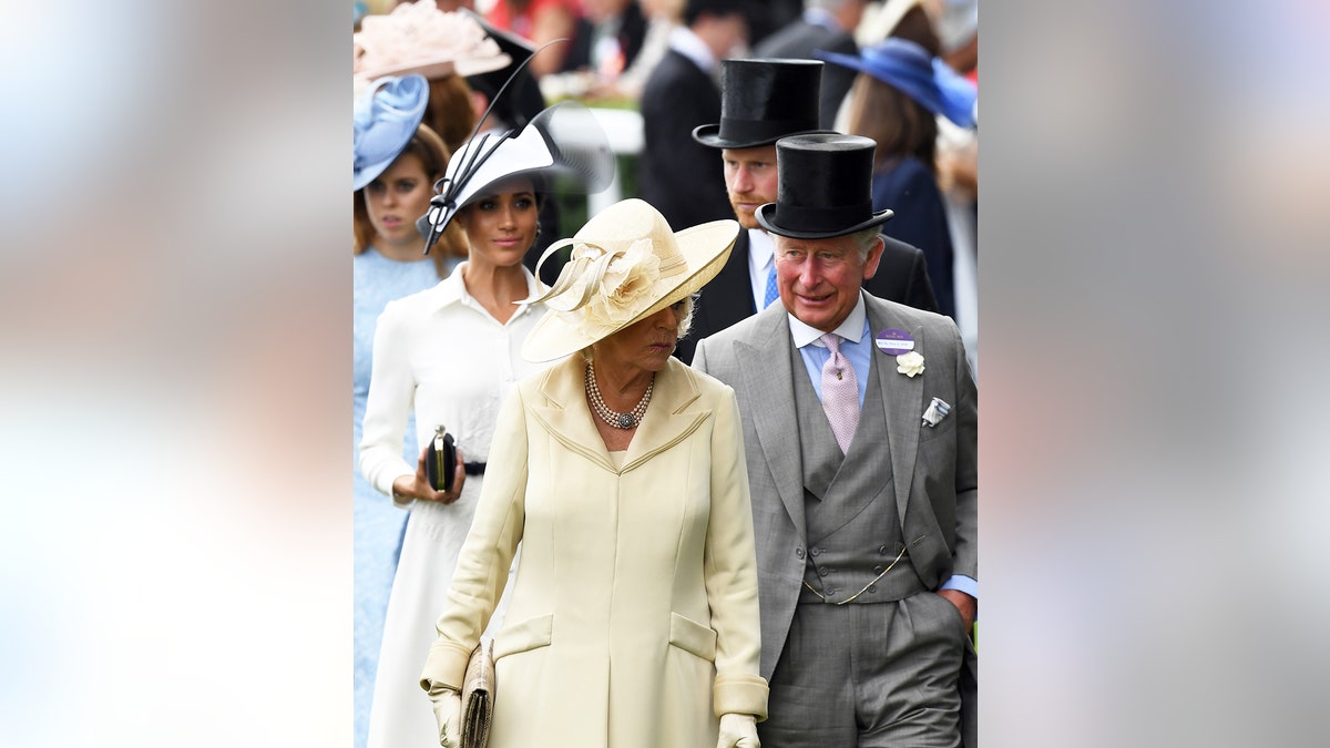 Prince Harry in a top hat and suit next to Meghan Markle in a white dress and a matching hat walking behind Queen Camilla in a yellow dress with a matching hat and King Charles in a grey suit and top hat