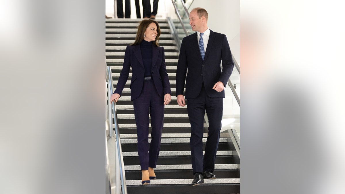 Prince William and Kate Middleton in matching black outfits walking down a flight of stairs