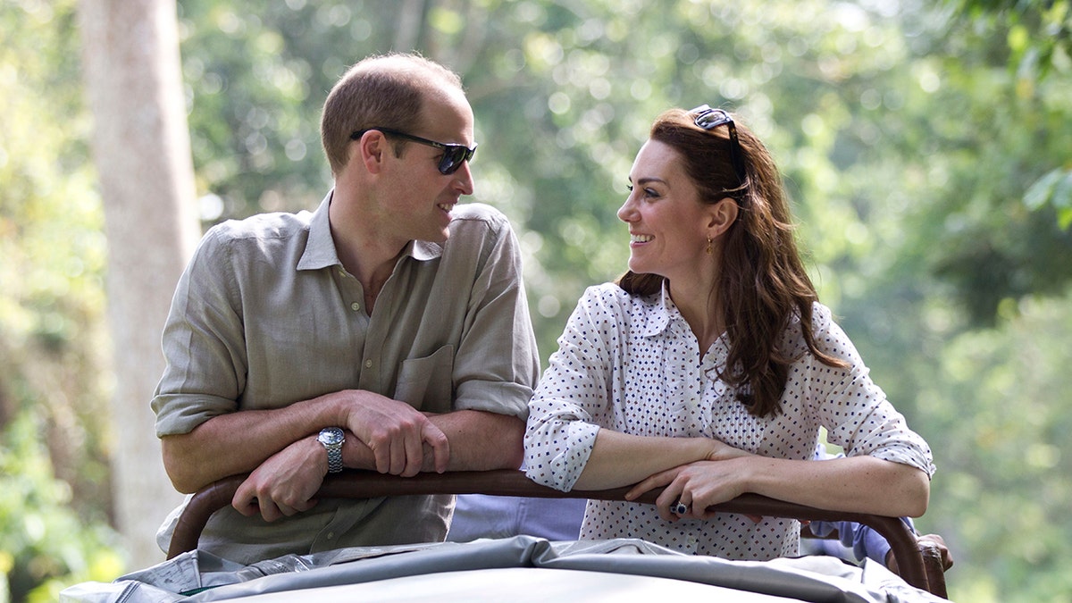 Prince William in a beige shirt and sunglasses looking at Kate Middleton in a white blouise