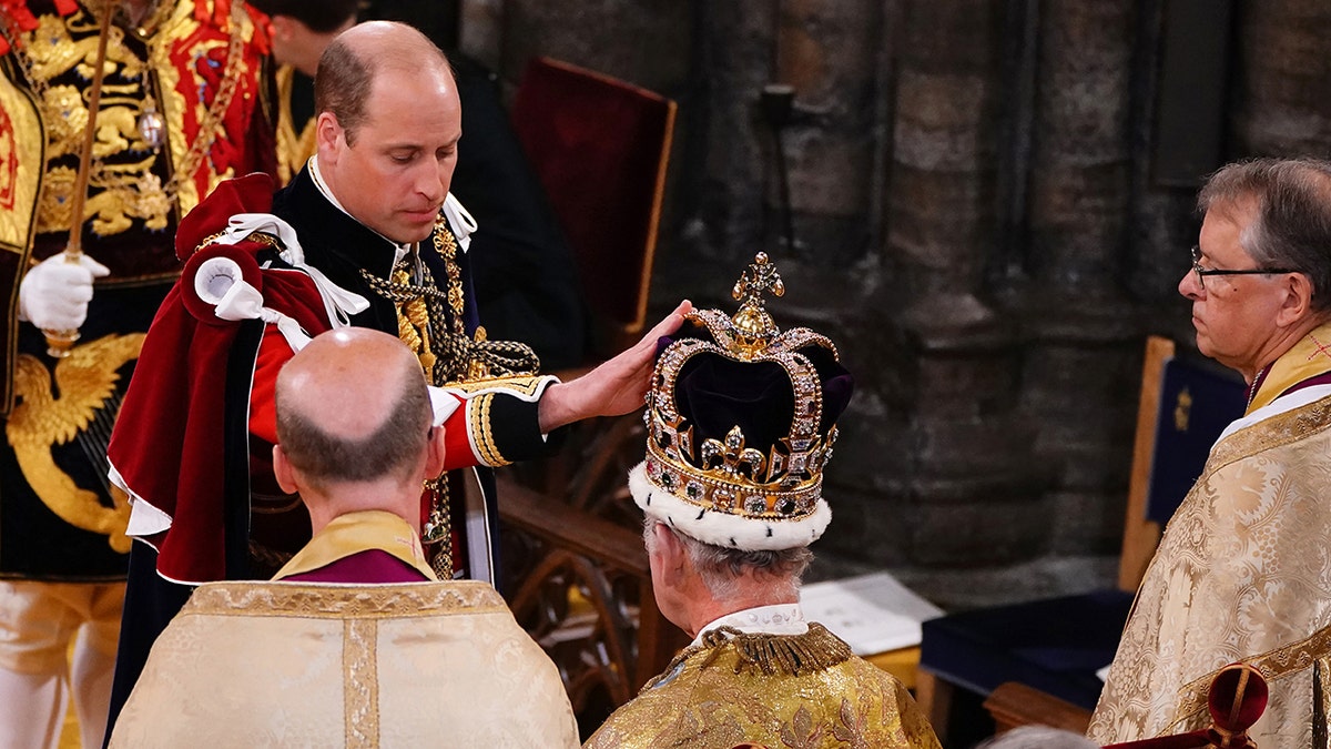 Prince William in royal regalia touching his father King Charles crown during the coronation ceremony