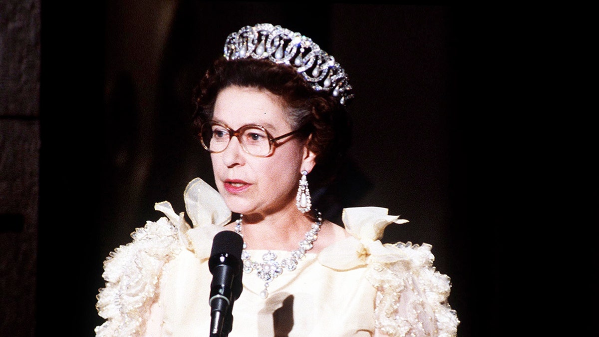 Queen Elizabeth wearing a white dress and glasses giving a speech