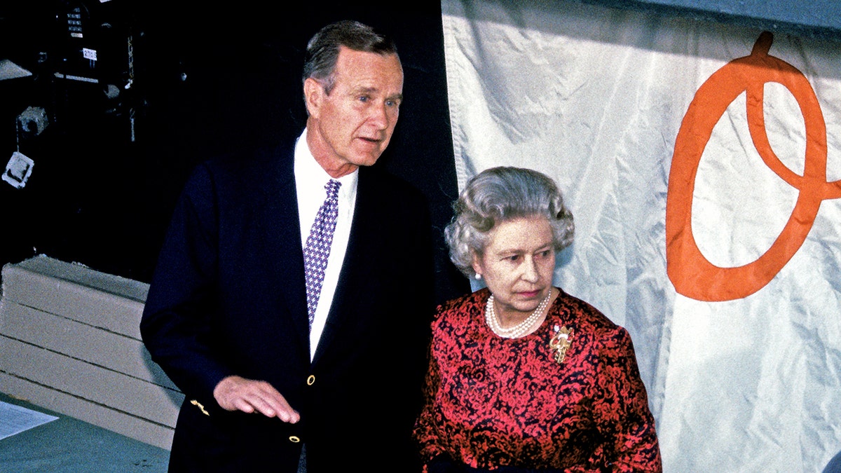 Queen Elizabeth wearing a red and black dress standing next to president bush