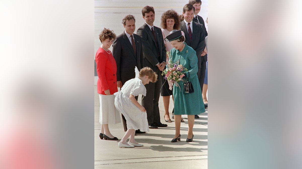 Queen Elizabeth wearing a green dress and holding a bouquet of flowers