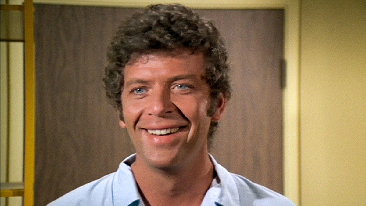A close-up of Robert Reed wearing a white shirt and smiling as Mike Brady
