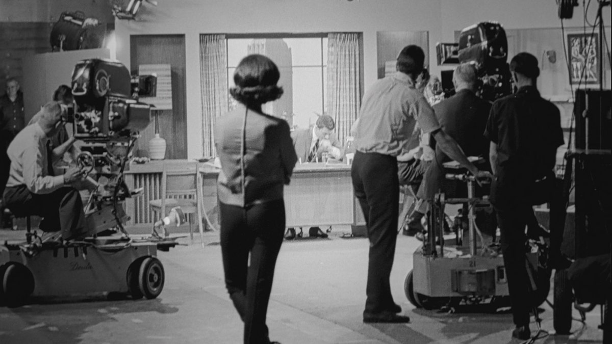 Mary Tyler Moore looking away from the camera on set wearing a long sleeved shirt and capri pants